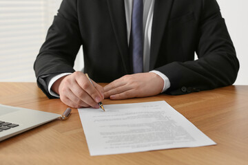 Notary signing document at wooden table indoors, closeup