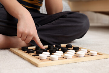 Playing checkers. Boy thinking about next move on floor in room, closeup
