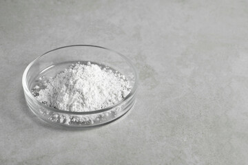 Petri dish with calcium carbonate powder on light grey table. Space for text