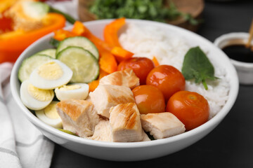 Delicious poke bowl with meat, rice, eggs and vegetables on black wooden table, closeup