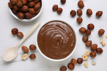 Bowl with chocolate paste and nuts on white marble table, flat lay