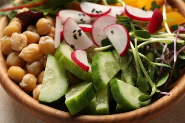 Delicious vegan bowl with cucumbers, chickpeas and radish on beige table, closeup