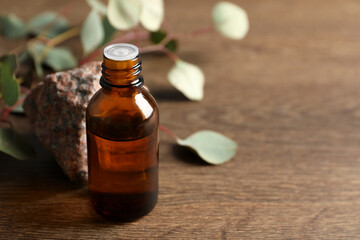 Bottle of eucalyptus essential oil, stone and leaves on wooden table. Space for text