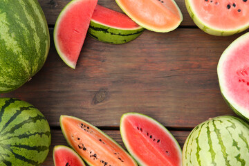 Frame made of different cut and whole watermelons on wooden table, flat lay. Space for text