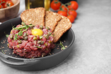 Tasty beef steak tartare served with yolk, capers and bread on light grey table. Space for text
