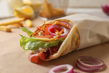 Delicious pita wrap with prosciutto and vegetables on parchment, closeup