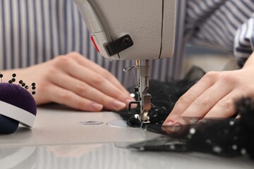 Dressmaker sewing new dress with machine in atelier, closeup