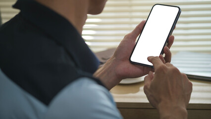 Cropped shot of man sitting in home office and using mobile phone. Blank screen for your text message or web design.