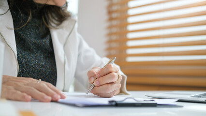 Close up view of senior woman writing down on a piece of paper, .making business plans at workplace.