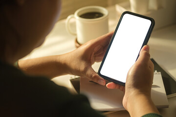 View over shoulder view of man using mobile phone at working desk. Blank phone screen for infographic and advertising.