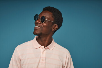 Minimal side view portrait of smiling black man wearing sunglasses against vibrant blue background, copy space