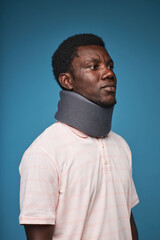 Vertical portrait of black man wearing neck brace against vibrant blue background, minimal