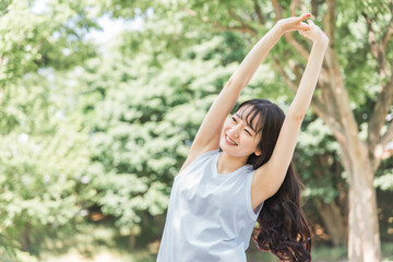 新緑の中でストレッチ・準備運動・深呼吸をする女性

