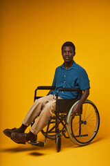 Vertical full length portrait of young black man using wheelchair and looking at camera in studio