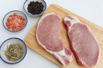 Organic raw pork meat on wooden chopping board with Himalayan pink salt, black pepper and dried rosemary. ingredients for cooking.Top view.