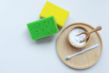 Baking soda (sodium bicarbonate) in wooden bowl, toothbrush and sponges on white background. Home...