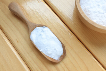 Top view of baking soda (sodium bicarbonate) with wooden spoon on wooden table. Home cleaning concept.