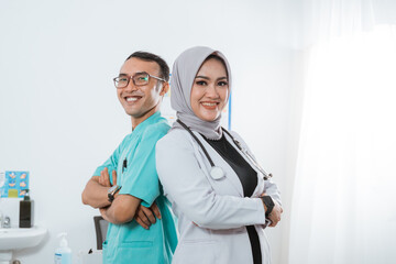 a beautiful doctor with grey veil standing with hand crossed back to back with the male nurse in nurse uniform inside the medical check up room