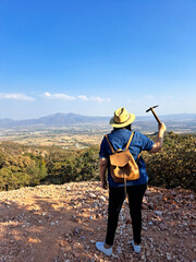 Latina woman with hat and miner's pick hammer works as a geologist, studies the composition and...