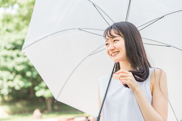 傘を差しながら髪を持つアジア人女性（ヘアケア）
