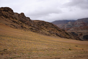 The gentle slope of a high rocky hill under thunderclouds in the autumn dried steppe.