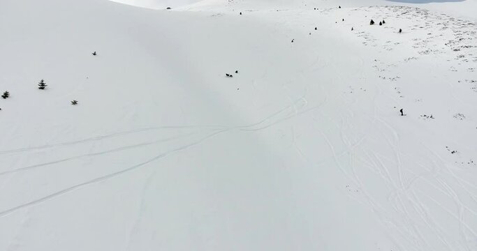 Freeride skier riding off-trail on fresh powder snow high in the mountains. Aerial view of extreme skiiing on the untouched terrain in snowy mountains.