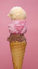 Vertical front view of vanilla ice cream on strawberry and chocolate ice cream cone on pink background.