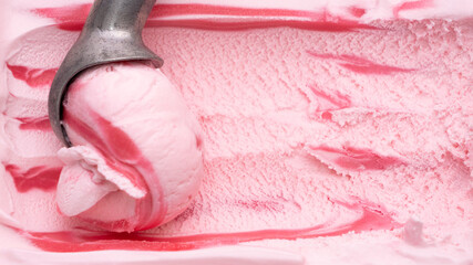 Close-up shot of steel spoon scooping up strawberry ice cream into round shapes.