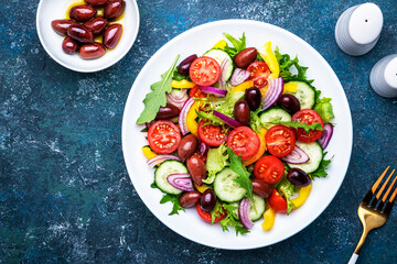 Vegan greek salad with kalamata olives, red tomato, yellow paprika, cucumber and onion, healthy mediterranean diet food, low calories eating. Blue stone background, top view