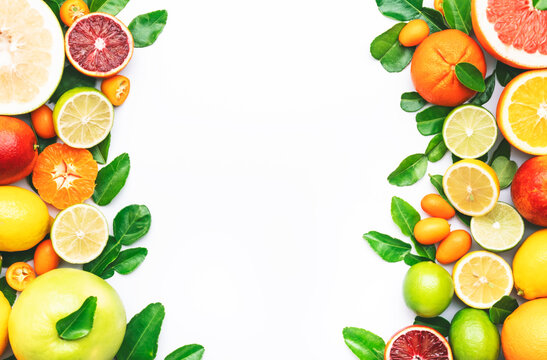 Citrus fruit food background, top view. Mix of different whole and sliced fruits: orange, grapefruit, lime and other with leaves on  white table, copy space border