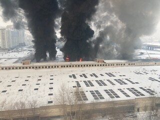 Large fire with black smoke. Burning industrial building, warehouse. A pillar of black smoke in the sky.