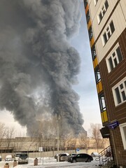 Large fire with black smoke. Burning industrial building, warehouse. A pillar of black smoke in the sky.