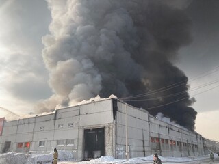 Large fire with black smoke. Burning industrial building, warehouse. A pillar of black smoke in the sky.