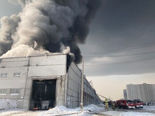 Large fire with black smoke. Burning industrial building, warehouse. A pillar of black smoke in the sky.