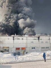 Large fire with black smoke. Burning industrial building, warehouse. A pillar of black smoke in the sky.