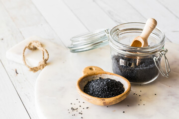 Black Hawaiian rock salt in a small bowl and jar, on a white marble board.