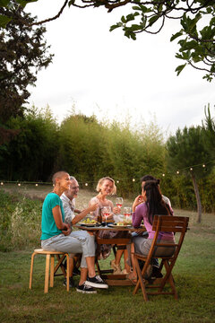 Happy friends laughing and eating at sunset during garden dinner party. Vertical image. Copy space.