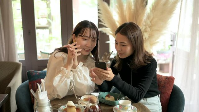 友達とカフェでスマートフォンをみて談笑する若い女性客