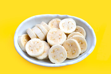 Banana slices in bowl on yellow background.