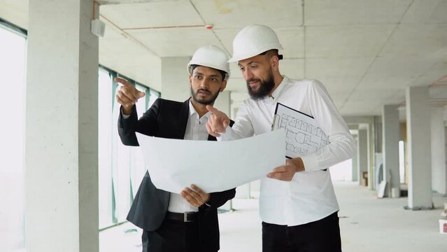 Indian architect and arabian supervisor meeting at construction site. Multiethnic engineers discussing on plan. Two construction workers working together while visiting a new building