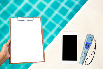 Digital water tester with smartphone and blank clipboard over swimming pool background, swimming...