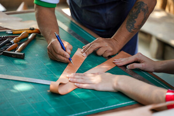 Closeup and crop team of leathers maker is drawing a design on leather in leather workshop.