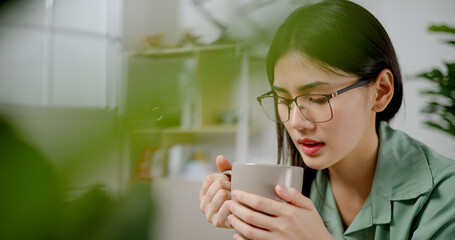 Portrait of Asian joyful young woman enjoying a cup of coffee at home