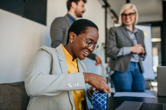The team celebrated a female colleague's birthday in the office during a meeting. Focus on a black businesswoman opening a gift