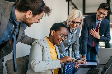 The team celebrated a female colleague's birthday in the office during a meeting. Focus on a black businesswoman opening a gift