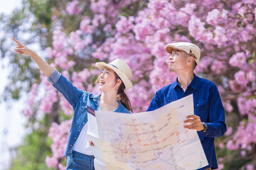 Asian couple tourist holding city map while walking in the park at cherry blossom tree during...