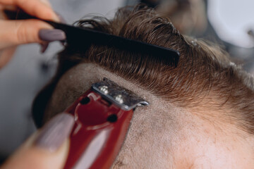 An approximate image of a man's head and a woman's hands holding an electric razor and a comb and carefully aligns the haircut.