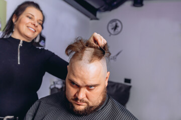 Hairdresser girl shaves hair from head of adult man completely. Getting rid of the hair on the head. Provision of services in a hairdressing salon.