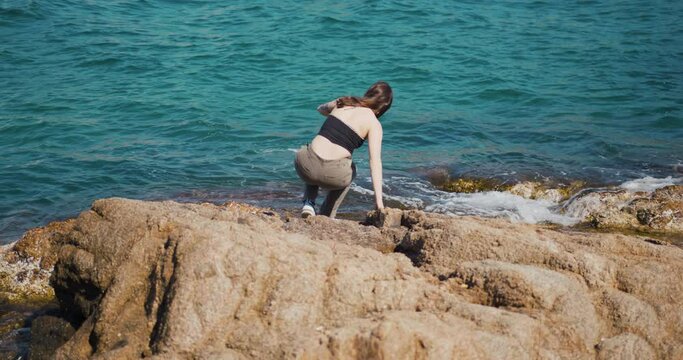 Girl looking at the ocean sitting on rocks