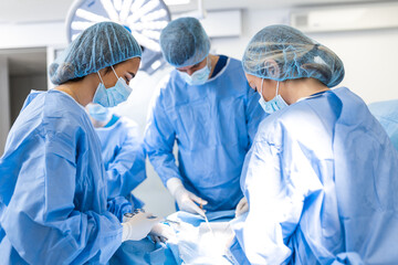 Medical team performing operation. Group of surgeon at work in operating theatre toned in blue. Doctor operation in operation room at hospital concept for insurance advertising. - obrazy, fototapety, plakaty